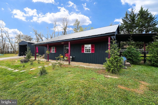 view of front facade with a front yard, metal roof, driveway, and an outbuilding