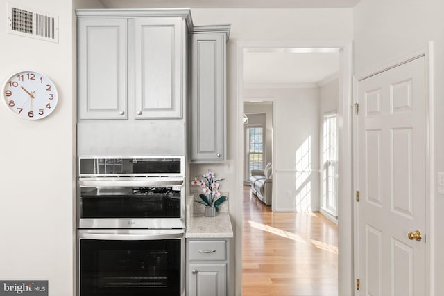 kitchen featuring gray cabinets, visible vents, double oven, ornamental molding, and light wood-type flooring