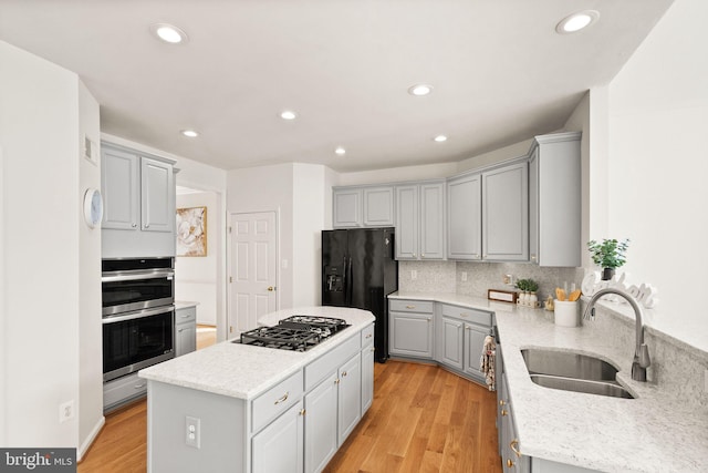 kitchen featuring a center island, stainless steel appliances, gray cabinets, a sink, and light wood-type flooring