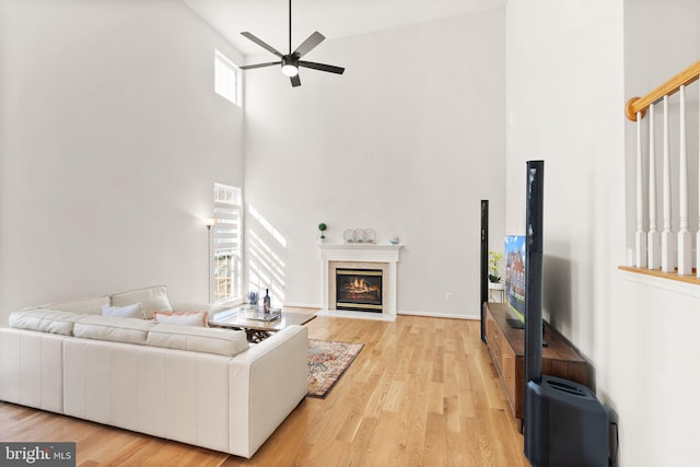 living area with visible vents, a high ceiling, a fireplace with flush hearth, a ceiling fan, and light wood-type flooring