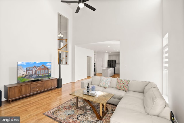 living room featuring a towering ceiling, wood finished floors, and ceiling fan with notable chandelier