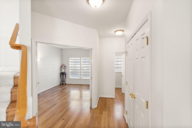 corridor featuring stairs, light wood-style flooring, and baseboards