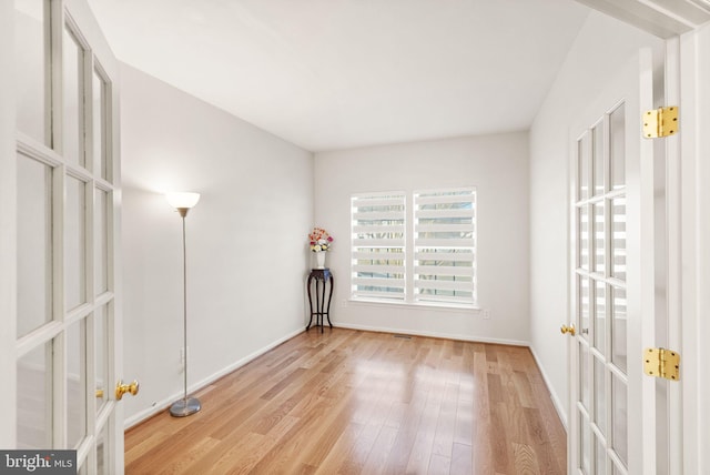 empty room featuring french doors, light wood-style flooring, and baseboards