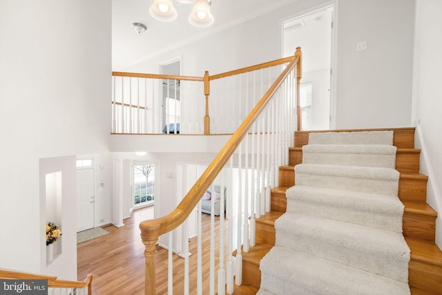 stairs with ornamental molding, a towering ceiling, and wood finished floors