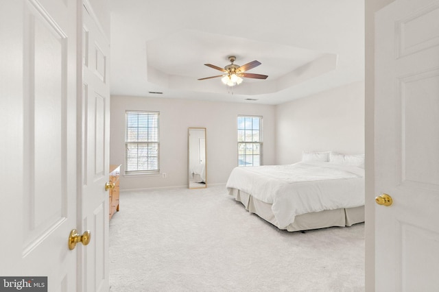 bedroom with baseboards, ceiling fan, a tray ceiling, and light colored carpet