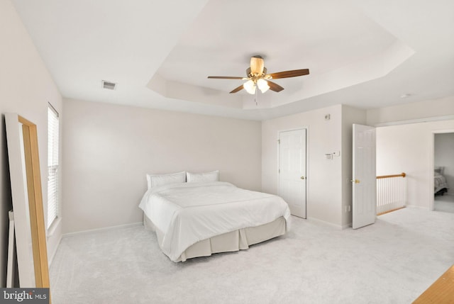 bedroom featuring light carpet, a tray ceiling, visible vents, and baseboards