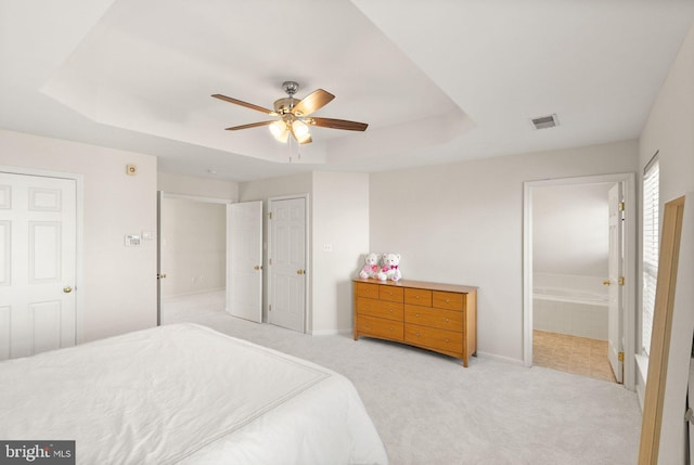 bedroom featuring light carpet, visible vents, a tray ceiling, and baseboards