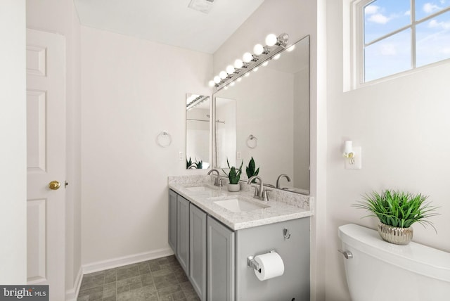 bathroom with double vanity, a sink, toilet, and baseboards