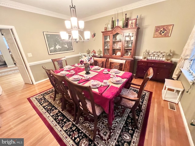 dining room featuring crown molding, wood finished floors, visible vents, baseboards, and an inviting chandelier