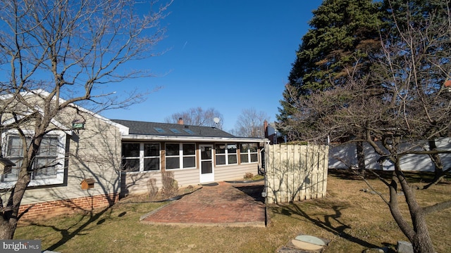 rear view of house featuring a shingled roof, fence, a lawn, a sunroom, and a patio