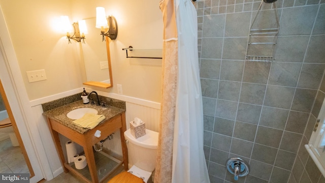 full bath featuring toilet, tiled shower, and a sink