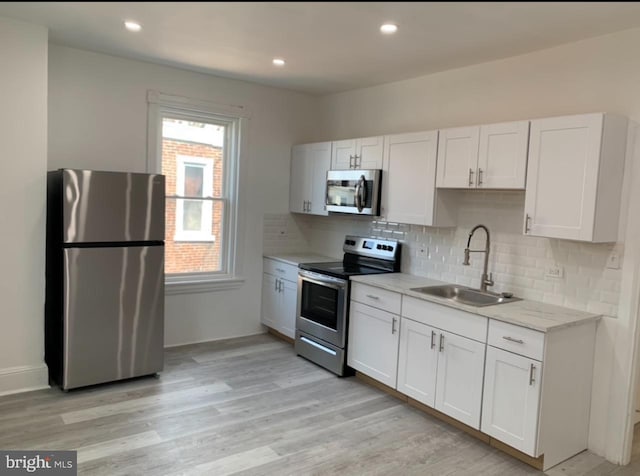 kitchen with appliances with stainless steel finishes, a sink, light wood-style flooring, and white cabinetry