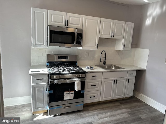 kitchen with light wood-style flooring, stainless steel appliances, light countertops, white cabinetry, and a sink