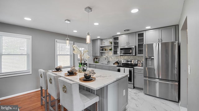 kitchen featuring backsplash, gray cabinetry, a kitchen bar, appliances with stainless steel finishes, and a sink