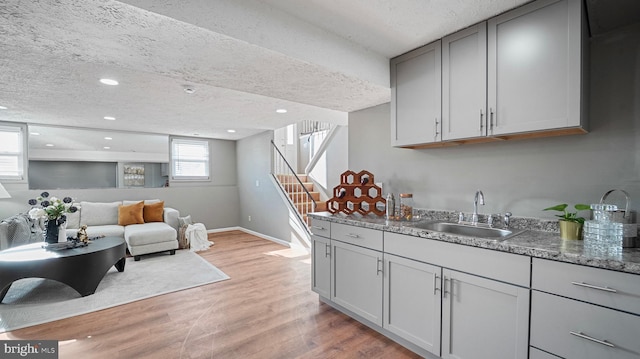 kitchen featuring stone counters, gray cabinetry, a sink, a textured ceiling, and light wood-type flooring