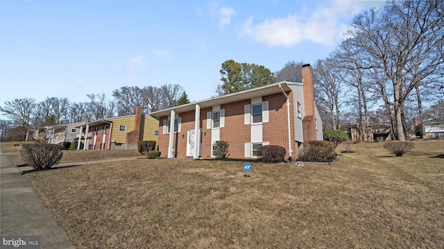 bi-level home featuring brick siding, a chimney, and a front lawn