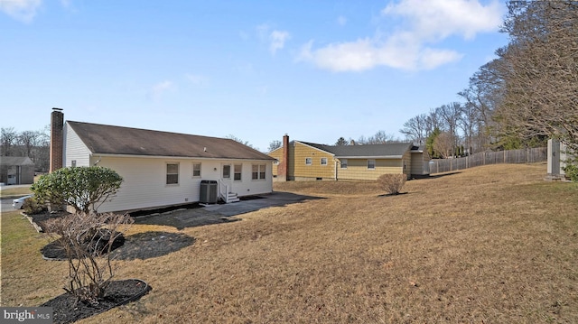 rear view of house with a chimney, central AC unit, fence, and a lawn