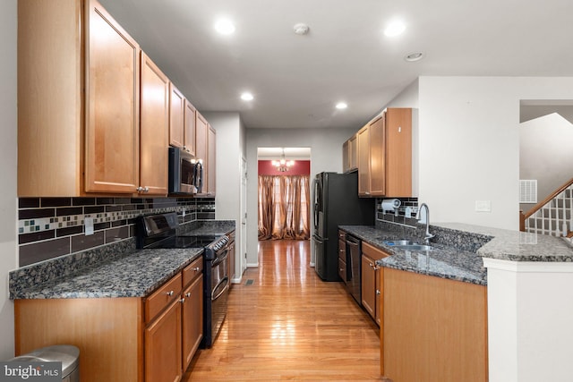 kitchen featuring sink, dark stone countertops, black appliances, light hardwood / wood-style floors, and kitchen peninsula