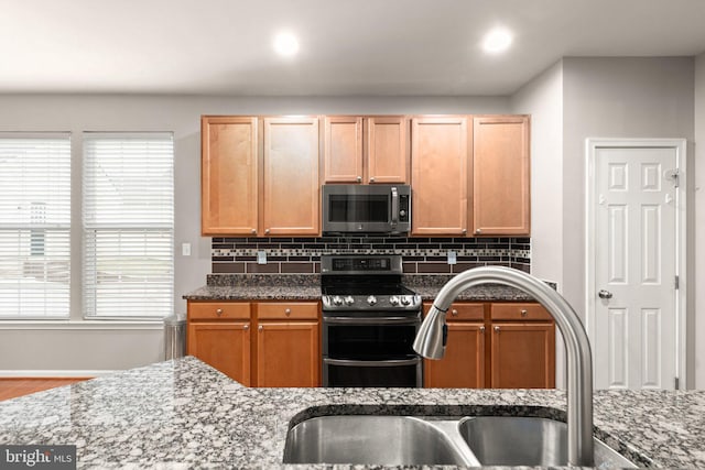 kitchen with stainless steel appliances, sink, decorative backsplash, and dark stone countertops