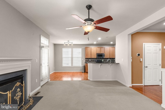 kitchen with light wood-type flooring, kitchen peninsula, ceiling fan, and decorative backsplash