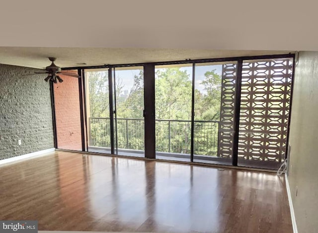 spare room with brick wall, wood finished floors, a wealth of natural light, and expansive windows