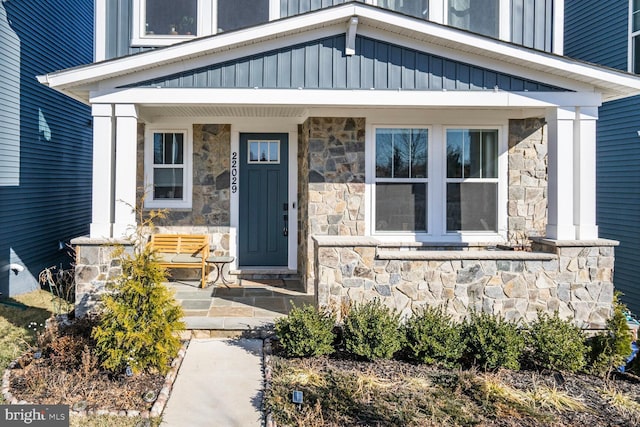 view of exterior entry featuring covered porch, stone siding, and board and batten siding