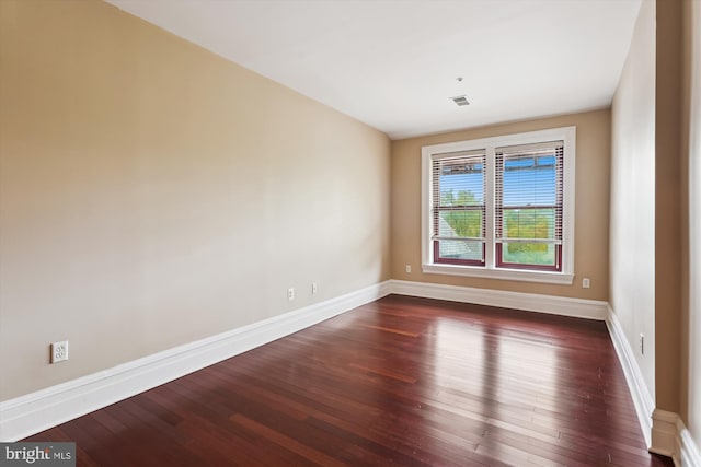 unfurnished room with baseboards, visible vents, and dark wood-style floors