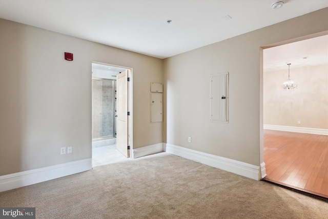 carpeted empty room with electric panel, baseboards, and an inviting chandelier