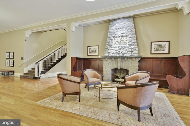 living area with wood finished floors, a stone fireplace, stairway, and ornamental molding
