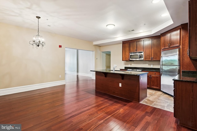 kitchen with stainless steel appliances, a breakfast bar, wood finished floors, a sink, and a notable chandelier