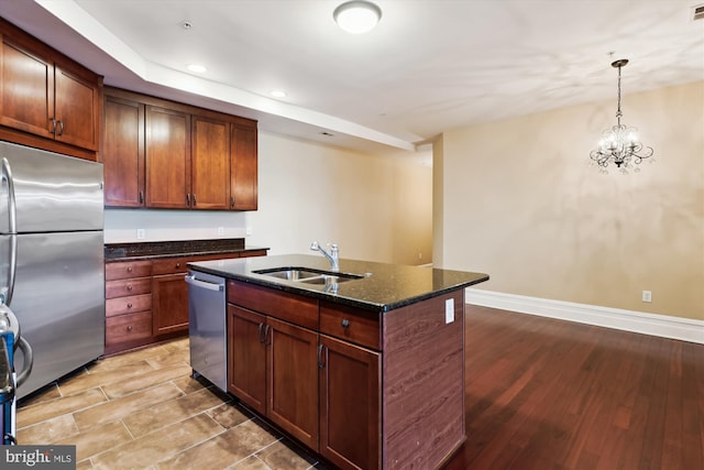 kitchen featuring stainless steel appliances, wood finished floors, a sink, and dark stone countertops