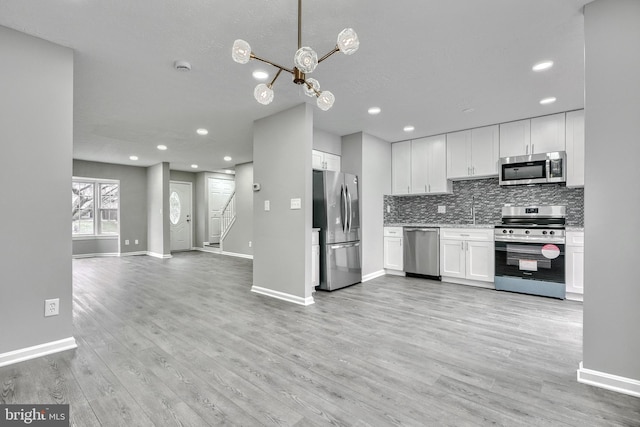 kitchen featuring appliances with stainless steel finishes, white cabinetry, light wood-type flooring, backsplash, and an inviting chandelier