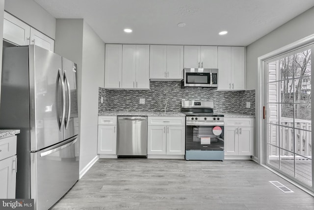 kitchen with tasteful backsplash, appliances with stainless steel finishes, white cabinets, and light hardwood / wood-style flooring