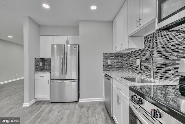 kitchen with white cabinetry, sink, light stone counters, stainless steel appliances, and light wood-type flooring