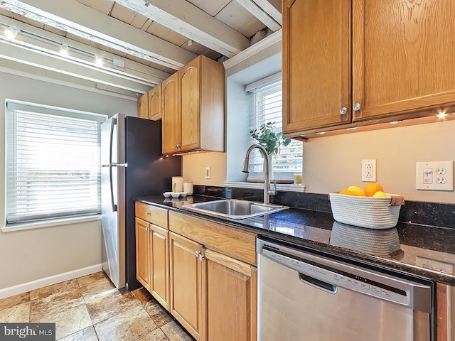 kitchen featuring appliances with stainless steel finishes, a sink, dark stone countertops, beamed ceiling, and baseboards