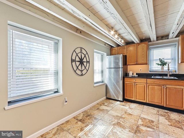 kitchen with a sink, baseboards, freestanding refrigerator, beamed ceiling, and dark countertops