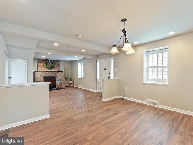 unfurnished living room with baseboards, visible vents, wood finished floors, a stone fireplace, and recessed lighting