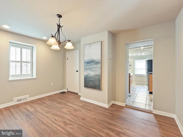 unfurnished dining area featuring an inviting chandelier, baseboards, visible vents, and wood finished floors