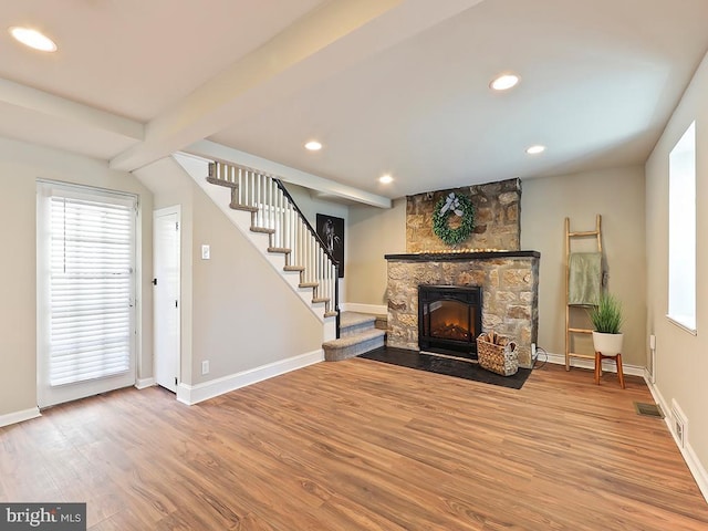 living area featuring beam ceiling, visible vents, a stone fireplace, wood finished floors, and stairs