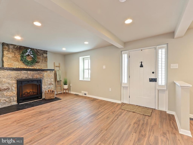 entryway featuring beam ceiling, a fireplace, visible vents, wood finished floors, and baseboards