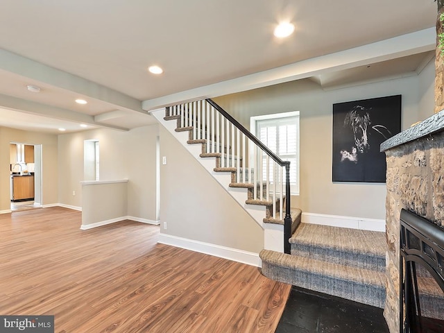 interior space featuring recessed lighting, a fireplace, wood finished floors, baseboards, and stairs