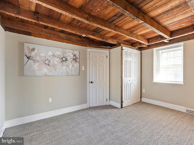 unfurnished bedroom featuring beamed ceiling, carpet flooring, wood ceiling, and baseboards