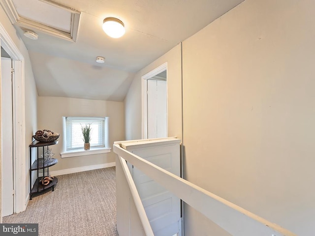 hallway with light colored carpet, attic access, vaulted ceiling, an upstairs landing, and baseboards