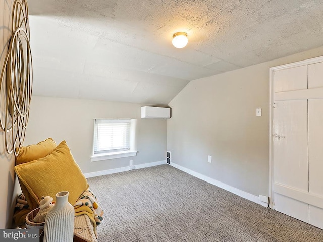 interior space with a textured ceiling, carpet flooring, baseboards, vaulted ceiling, and an AC wall unit