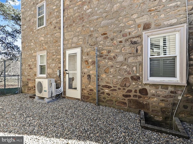 view of exterior entry with stone siding, ac unit, and fence