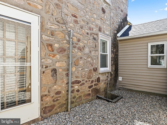 view of exterior entry featuring stone siding and roof with shingles