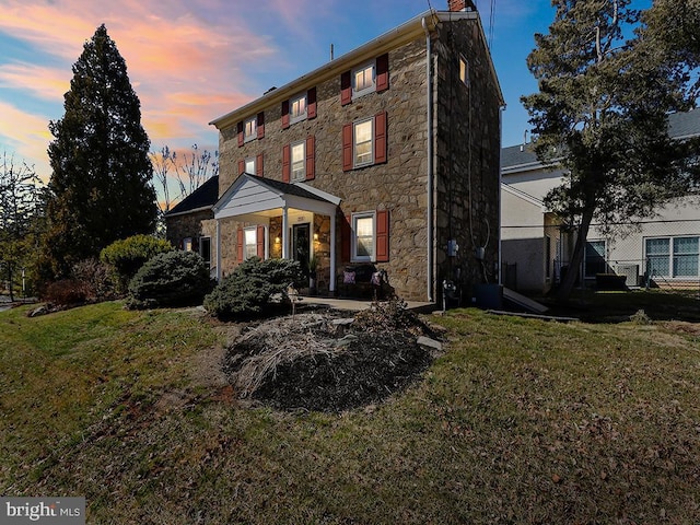 exterior space featuring stone siding, a chimney, and a front lawn