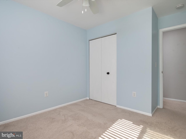 unfurnished bedroom featuring baseboards, ceiling fan, a closet, and light colored carpet