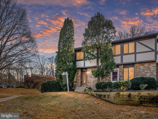 view of front of house featuring brick siding, a yard, and stucco siding