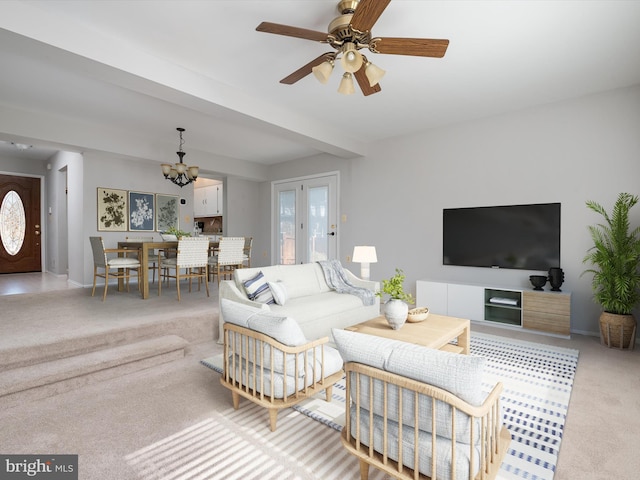 living room featuring light colored carpet, baseboards, and ceiling fan with notable chandelier